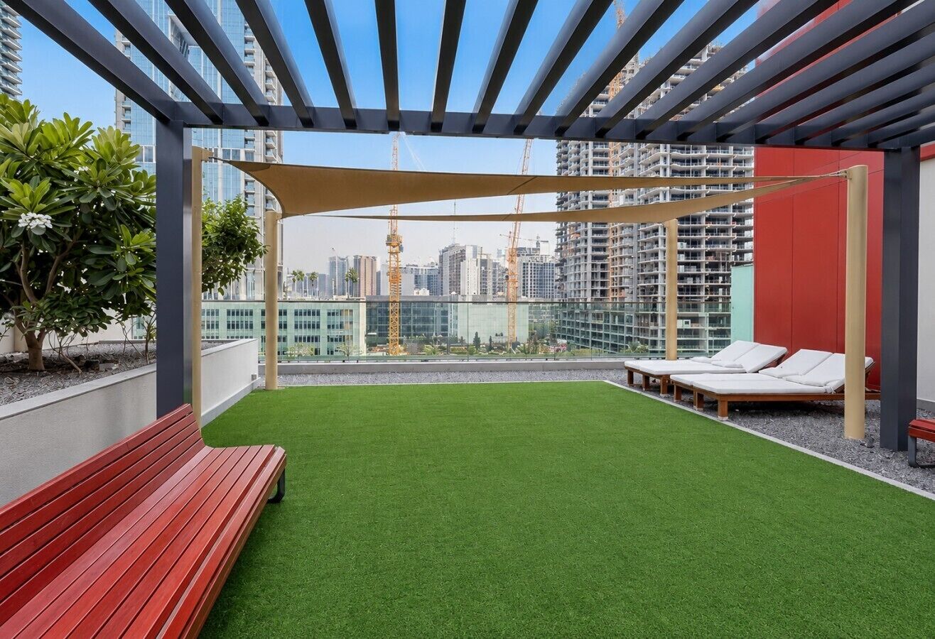 Een terras op het dak met kunstgras, een rode bank en lounge fauteuils.