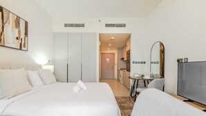 A hotel room with a large bed, a TV, a desk, and a kitchenette. - HAVN - Studio in JVC with Pool View (Dubai)