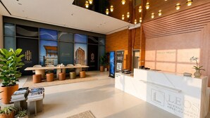 A modern reception area with a reception desk, seating area, and potted plants. - HAVN - Studio in JVC with Pool View (Dubai)