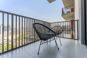 A balcony with a view of a cityscape, featuring two black wireframe chairs and a tiled floor. - HAVN - Studio in JVC with Pool View (Dubai)