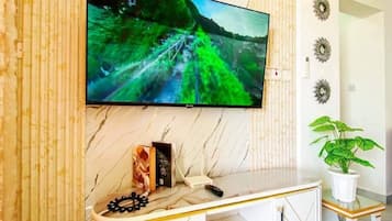 Una sala de estar moderna con un televisor de pantalla plana montado en una pared de mármol, un mueble de entretenimiento blanco y dorado, y una planta en maceta.