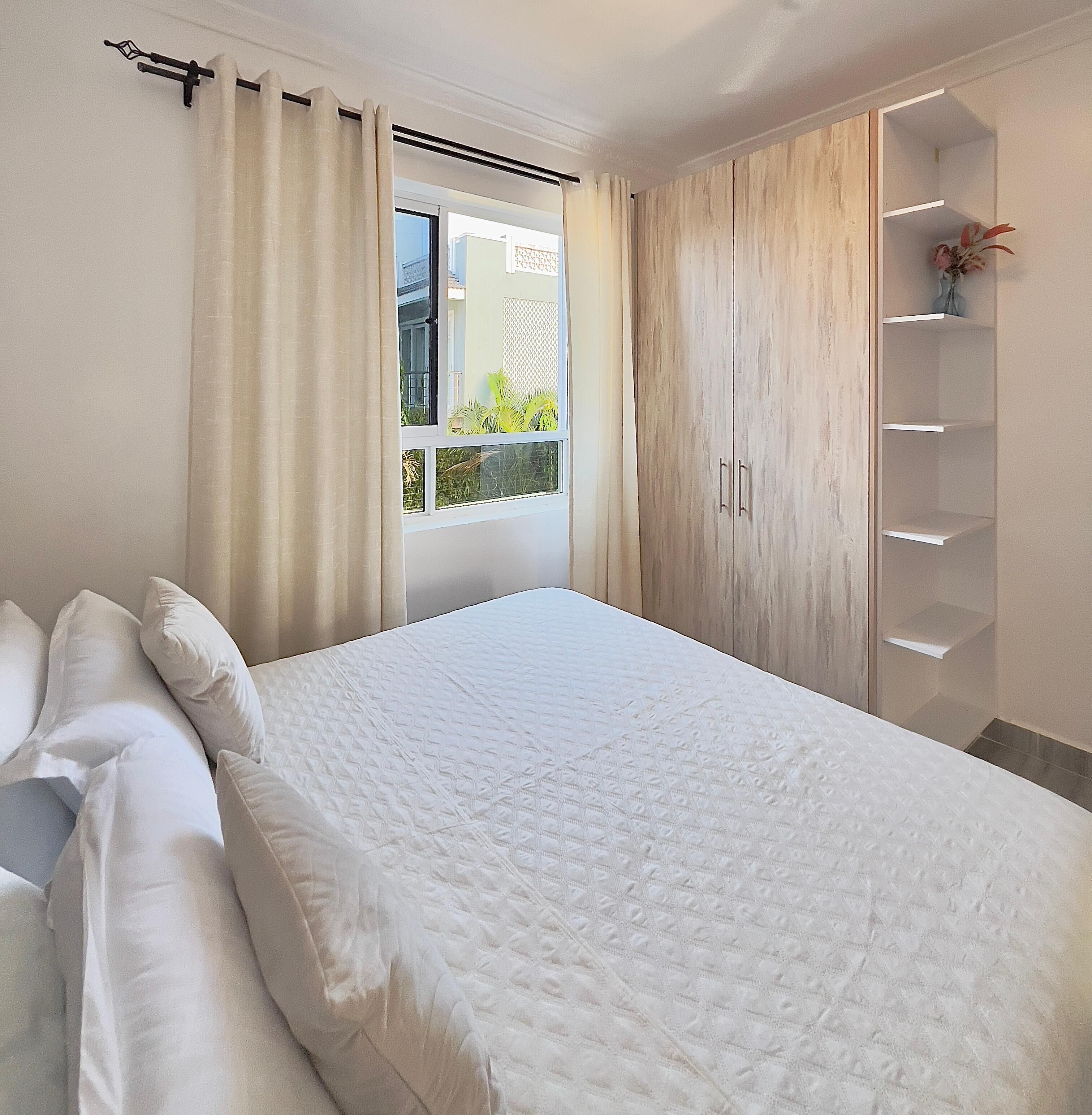 Un dormitorio con cama, cortinas, una ventana y un armario.
