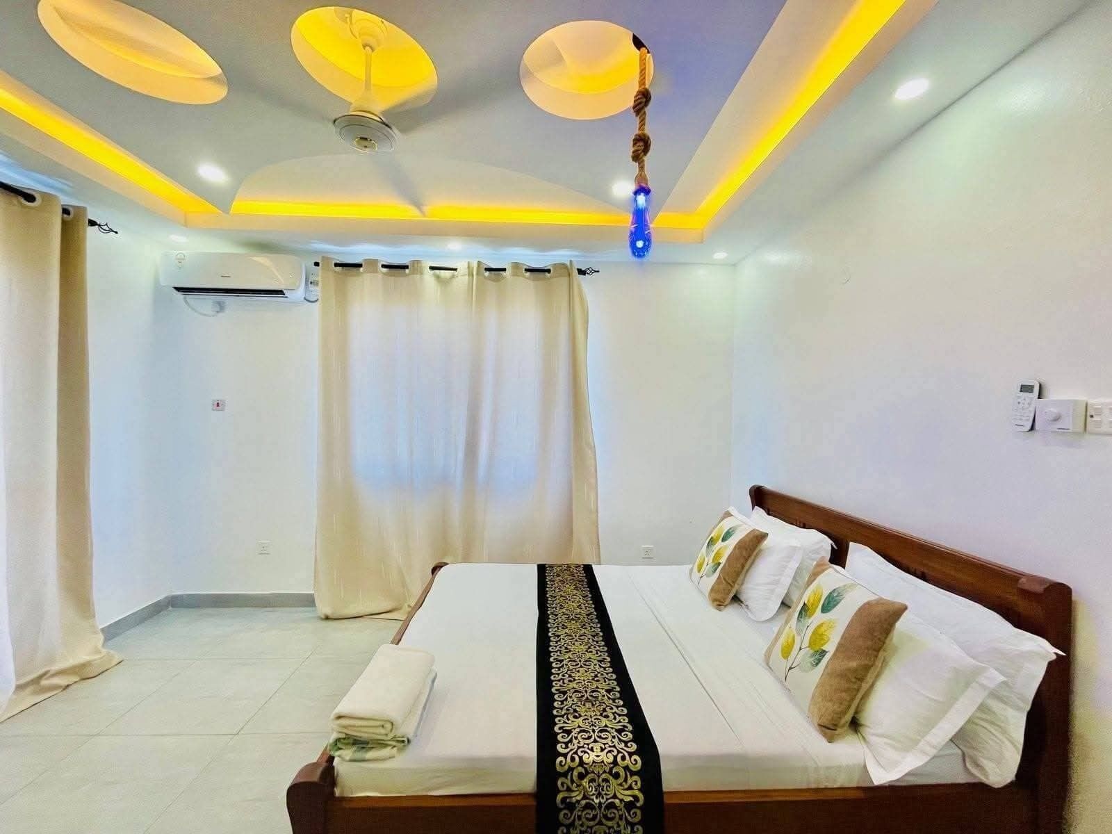 Una habitación de hotel con cama, cortinas, luces de techo y aire acondicionado instalado en la pared.