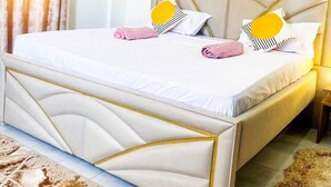 Una cama bien hecha con cabecera, aire acondicionado de pared y cuadros colgados encima.