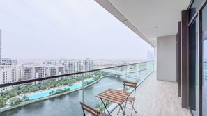 A balcony with a view of a river and buildings, a glass railing, and a wooden table and chairs. - Palace Residences - Dubai Creek Harbour (Dubai)