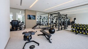 A modern gym with various exercise equipment, a large mirror, and a bench. - Palace Residences - Dubai Creek Harbour (Dubai)