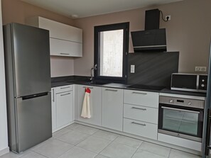 A modern kitchen with a refrigerator, oven, microwave, and a window. - Cozy apartment for 5 people, 500 meters from the beach and 350 meters from downtown (Biscarrosse)