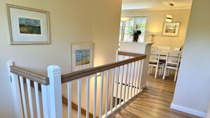 A staircase with white railings and a wooden handrail leading to a dining area with white chairs and a table. - Eidumweg Apartment 2 - Modern vacation rental with a terrace, sauna, and amenities for 3 (Sylt)