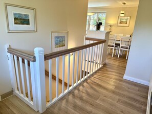 A staircase with white railings and a wooden handrail leading to a dining area with white chairs and a table. - Eidumweg Apartment 2 - Modern vacation rental with a terrace, sauna, and amenities for 3 (Sylt)