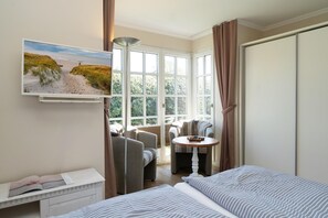 Ein Hotelzimmer mit Bett, Schreibtisch, Stuhl, Tisch und einem großen Fenster mit Vorhängen.