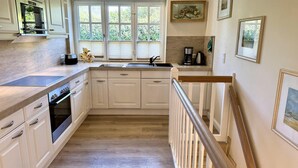A kitchen with white cabinets, a wooden countertop, a built-in oven, a sink, and a staircase with a wooden railing. - Eidumweg Apartment 2 - Modern vacation rental with a terrace, sauna, and amenities for 3 (Sylt)