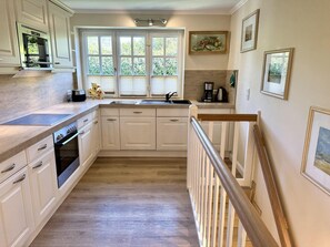 A kitchen with white cabinets, a wooden countertop, a built-in oven, a sink, and a staircase with a wooden railing. - Eidumweg Apartment 2 - Modern vacation rental with a terrace, sauna, and amenities for 3 (Sylt)