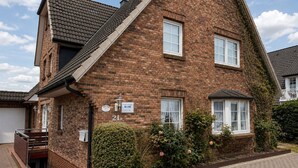 A two-story brick house with a visible number '21a' indicating its address. - Kampstraße, Apartment 4a - Cozy 3-room vacation apartment with 2 balconies in a quiet (Sylt)