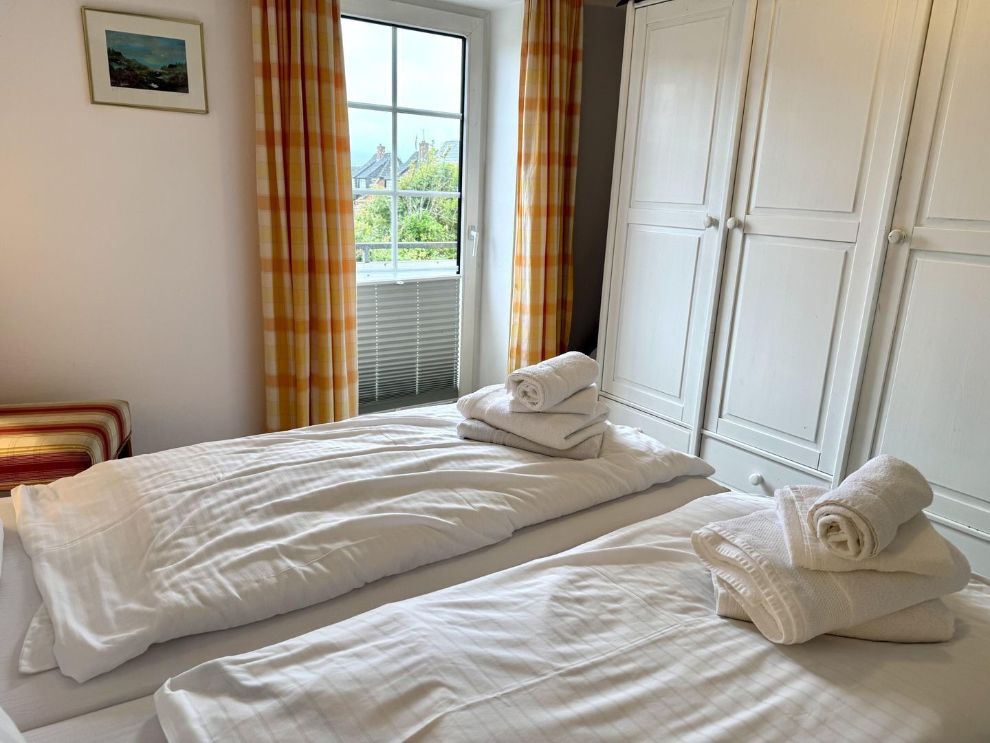 A bedroom with two beds, a wardrobe, and a window with curtains.