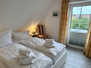 Quarto de hotel com cama, poltrona, mesa de cabeceira, abajur, quadro na parede e janela com cortinas.