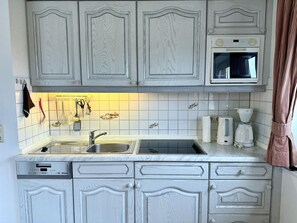 A kitchen with white cabinetry, a built-in microwave, and a coffee maker. - Kampstraße, Apartment 4a - Cozy 3-room vacation apartment with 2 balconies in a quiet (Sylt)