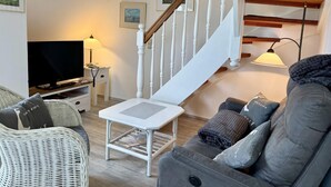 A living room with a sofa, a television, a lamp, a staircase, and framed pictures on the wall. - Kampstraße, Apartment 4a - Cozy 3-room vacation apartment with 2 balconies in a quiet (Sylt)