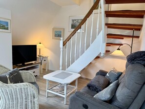 Uma sala de estar com um sofá, uma televisão, um abajur, uma escada e quadros nas paredes.
