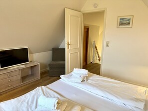 A bedroom with a bed, a TV, a chair, and a door leading to another room. - Kampstraße, Apartment 4a - Cozy 3-room vacation apartment with 2 balconies in a quiet (Sylt)