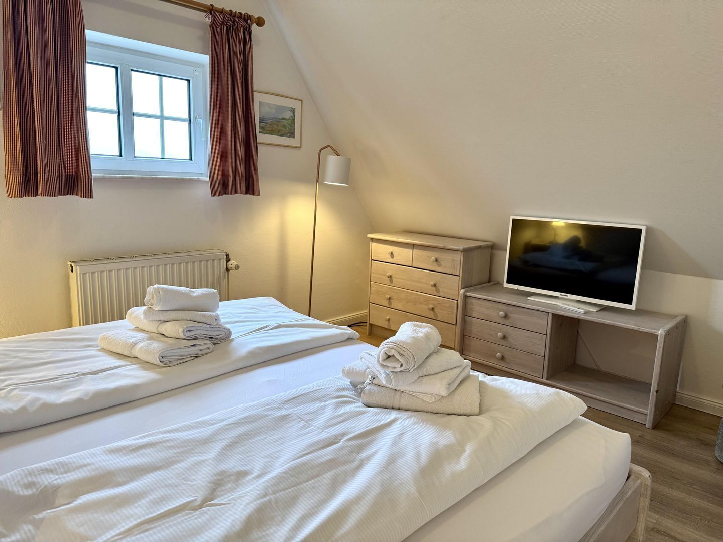 Une chambre d’hôtel avec un lit, une télévision, une commode et une fenêtre avec des rideaux.