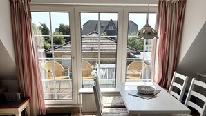 A dining area with a table and chairs, a view of the outside, and a window with curtains. - Süderstraße, Apartment 12 – Landhaus - Cozy 3-room vacation rental for 4 (Sylt)