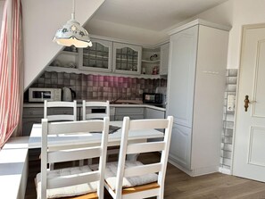 A compact kitchen with white cabinetry, a dining table with chairs, and a hanging light fixture. - Süderstraße, Apartment 12 – Landhaus - Cozy 3-room vacation rental for 4 (Sylt)