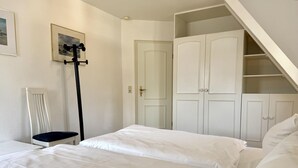A bedroom with two beds, a chair, a coat rack, and a wardrobe. - Süderstraße, Apartment 12 – Landhaus - Cozy 3-room vacation rental for 4 (Sylt)