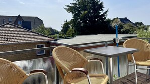 A rooftop terrace with wicker chairs and a table, overlooking a residential area with houses and a large tree. - Süderstraße, Apartment 12 – Landhaus - Cozy 3-room vacation rental for 4 (Sylt)