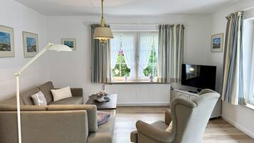 En stue med sofa, lænestol, fjernsyn og et vindue med gardiner.