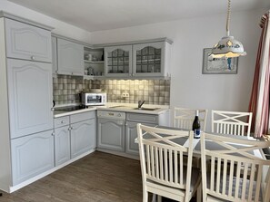 A kitchen with white cabinetry, a microwave, a sink, and a dining area with a table and chairs. - Süderstraße, Apartment 09 – Landhaus - Cozy 2-room vacation rental for 4 (Sylt)