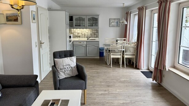 A modern living room with a grey sofa, a white coffee table, and a dining area with a white table and chairs. - Süderstraße, Apartment 09 – Landhaus - Cozy 2-room vacation rental for 4 (Sylt)