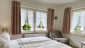 A bedroom with two beds, a chair, and windows with curtains. - Süderstraße, Apartment 09 – Landhaus - Cozy 2-room vacation rental for 4 (Sylt)