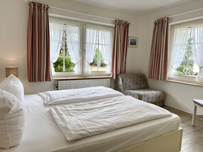 Ein Schlafzimmer mit zwei Betten, einem Sessel und Fenstern mit Vorhängen.