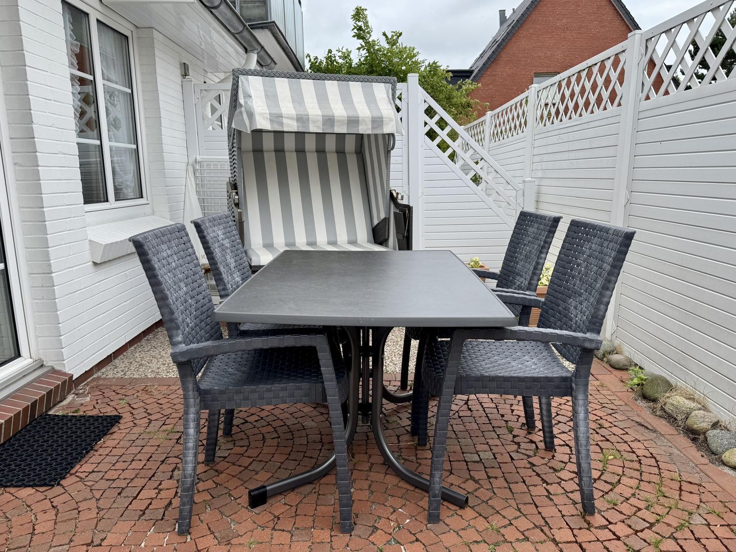 Une terrasse avec une table et des chaises, un auvent à rayures et une clôture blanche.