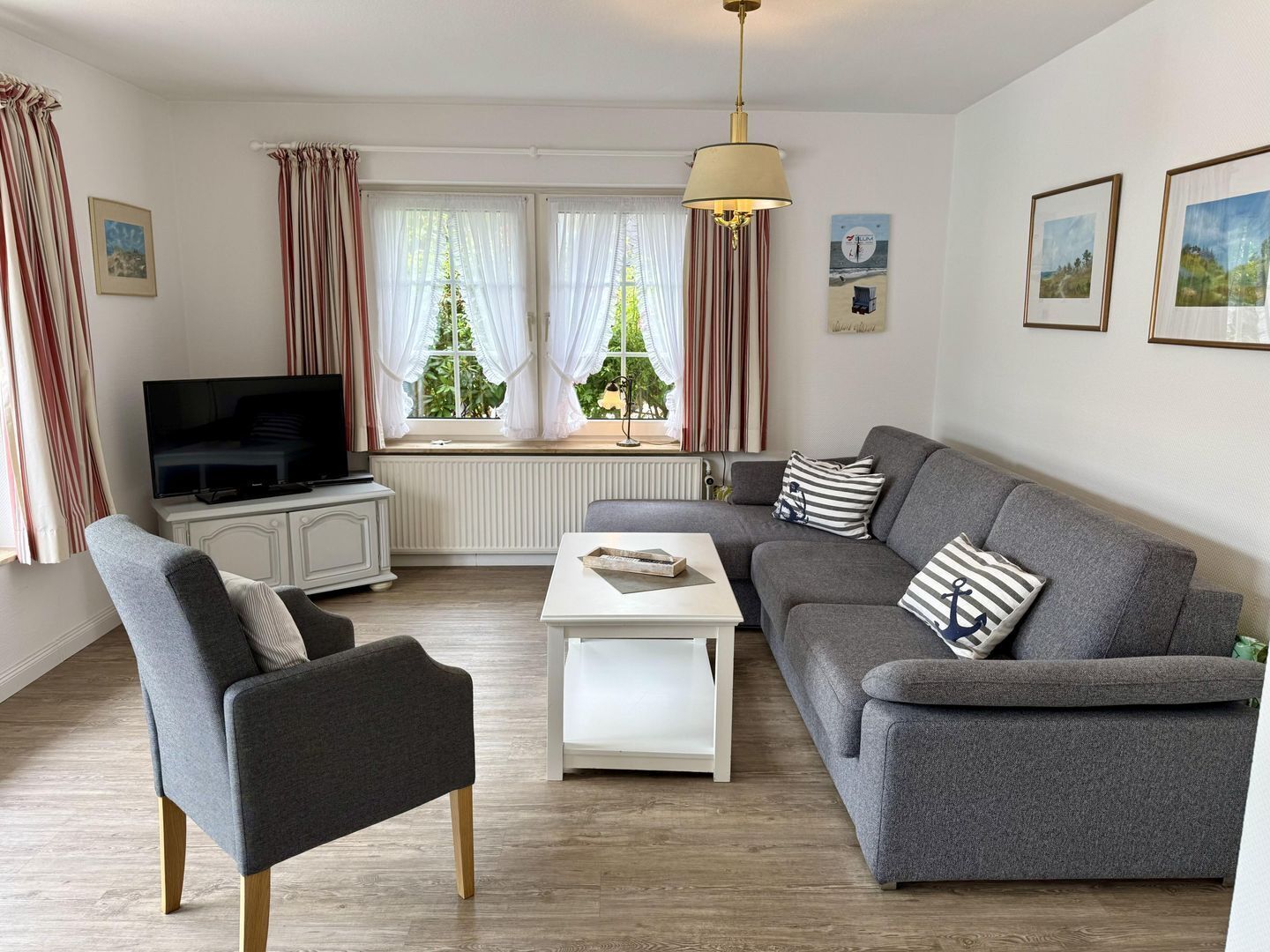 Un salón moderno con un sofá gris, una mesa de centro blanca y un televisor sobre un mueble blanco.