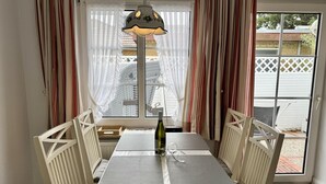 A dining area with a table and chairs, a bottle of wine, and a view through a window. - Süderstraße, Apartment 09 – Landhaus - Cozy 2-room vacation rental for 4 (Sylt)