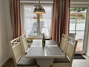 Ein Essbereich mit Tisch und Stühlen, einer Weinflasche und Blick durch ein Fenster.