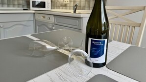 A bottle of wine and two glasses on a table in a kitchen with a tiled backsplash and a microwave. - Süderstraße, Apartment 09 – Landhaus - Cozy 2-room vacation rental for 4 (Sylt)