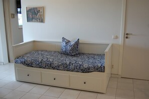 A single bed with a floral-patterned bedspread and a matching pillow, positioned against a white wall with a door to the right. - Charming villa with 3 bedrooms and sea view (Santa Bárbara de Nexe)