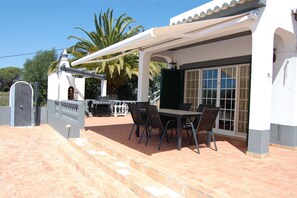 An outdoor patio with a grill, dining table, and chairs. - Charming villa with 3 bedrooms and sea view (Santa Bárbara de Nexe)