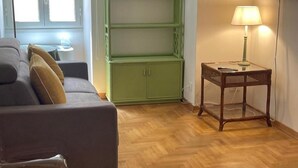 Ein Wohnzimmer mit einer Couch, einem grünen Schrank, Holzdielen und einem Tisch mit einer Lampe.