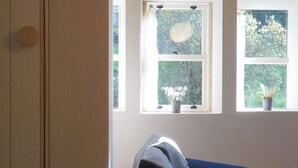 A room with a blue sofa, a dining table, and two windows with potted plants. - Triangle Cottage - A beautifully restored and furnished luxury cottage for two (Hebden Bridge)
