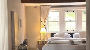 A bedroom with a bed, a bedside table with a lamp, a mirror, and a window with curtains. - Triangle Cottage - A beautifully restored and furnished luxury cottage for two (Hebden Bridge)