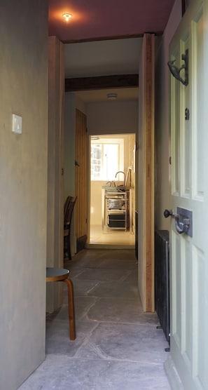 A hallway leading to a kitchen with a window, a radiator, and a chair.