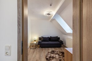 A modern loft bedroom with a sloped ceiling, a dark sofa, a small table with a lamp, and a shaggy rug.