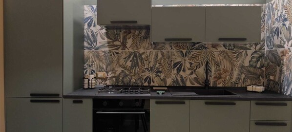 A kitchen with a gas stove, oven, and a backsplash with a tropical leaf pattern. - Elegant downtown apartment with a hot tub and a view of Naples (Napoli)