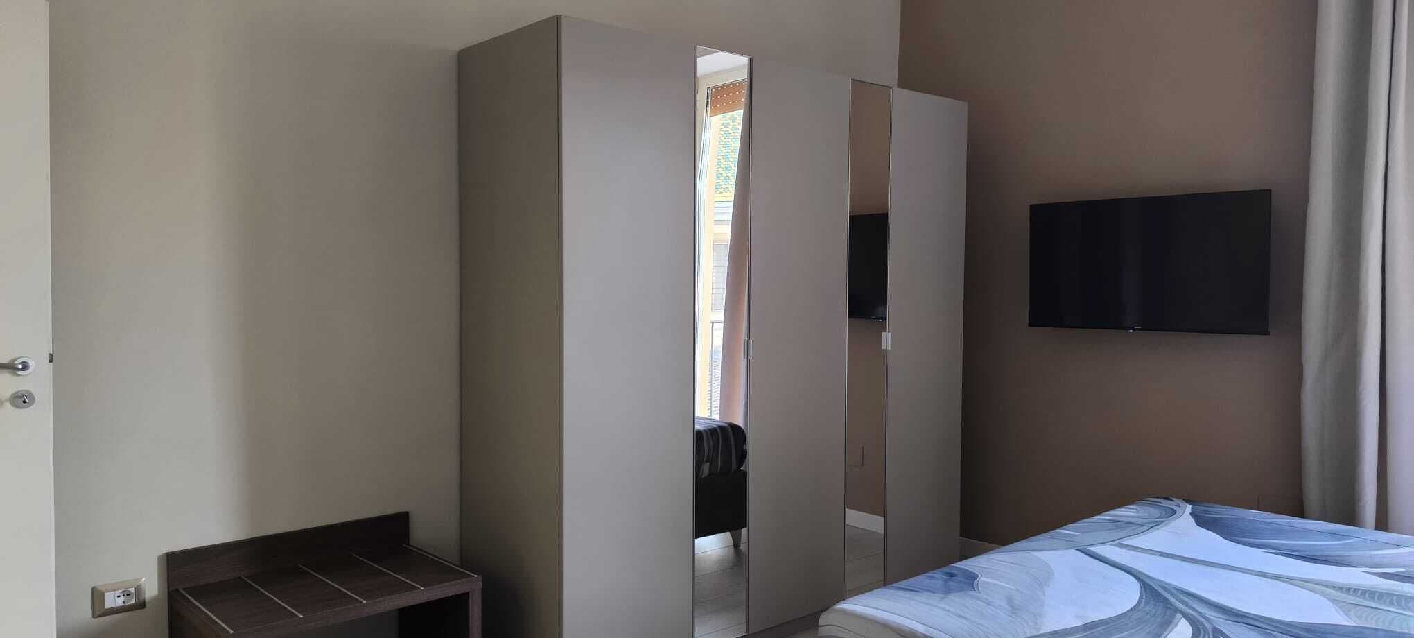 Ein Hotelzimmer mit Bett, Kleiderschrank, Fernseher und einem kleinen Tisch.