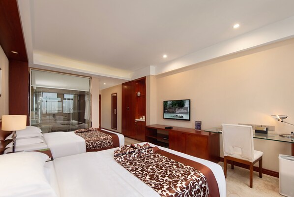 Habitación de hotel con dos camas, un escritorio, una silla, un televisor y un separador de vidrio.