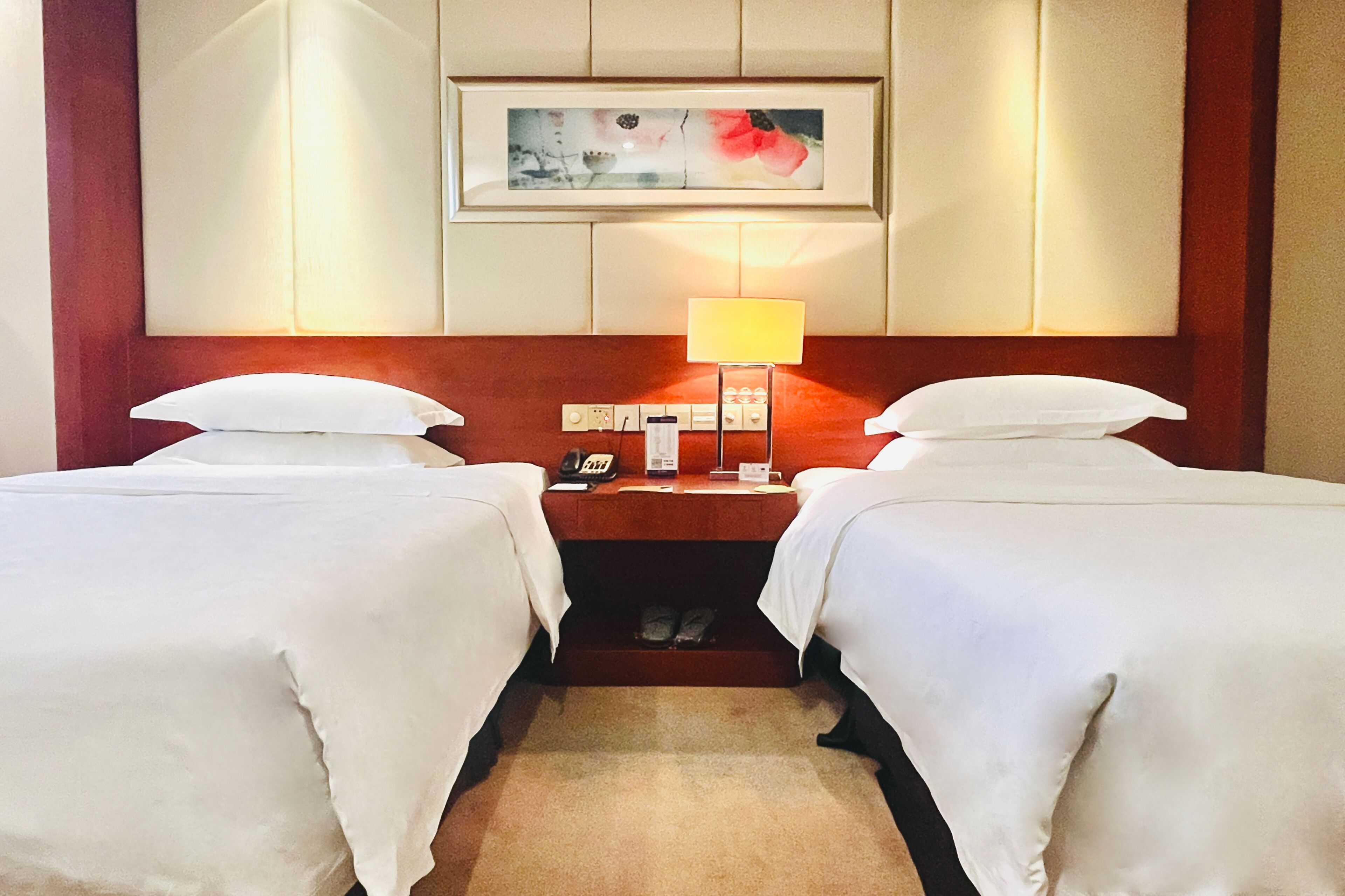Habitación de hotel con dos camas, una mesita de noche con lámpara, teléfono y un cuadro en la pared.