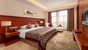 A hotel room with a large bed, bedside tables, a desk, a chair, and a television.